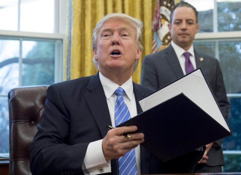 US President Donald Trump signs an executive order alongside White House Chief of Staff Reince Priebus (R) in the Oval Office of the White House in Washington, DC, January 23, 2017.Trump on Monday signed three orders on withdrawing the US from the Trans-Pacific Partnership trade deal, freezing the hiring of federal workers and hitting foreign NGOs that help with abortion. Photo credit: SAUL LOEB/AFP/Getty Images
